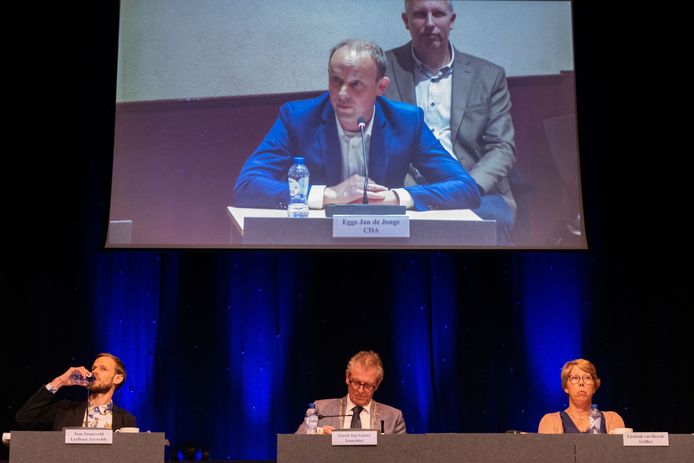 Wat een feest van de democratie zou moeten zijn werd een kille vergadering, waarin Tom Zonneveld van Leefbaar Zeewolde (l) felle kritiek kreeg van onder andere burgemeester Gerrit Jan Gorter (midden) en Egge Jan de Jonge van het CDA (op het scherm). Rechts in beeld: raadsgriffier Liesbeth van Heezik.
