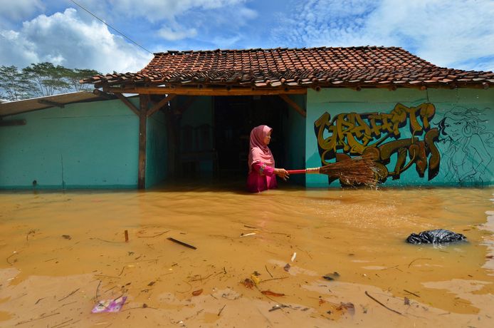 Een Indonesische vrouw verwijdert met een bezem wat rommel uit het water tijdens een fikse overstroming in Tasikmalaya. Foto Adeng Bustomi