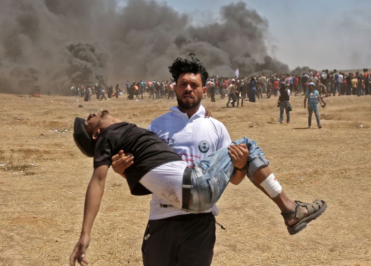 Een Palestijn draagt een gewonde betoger weg van het slagveld. Beeld AFP
