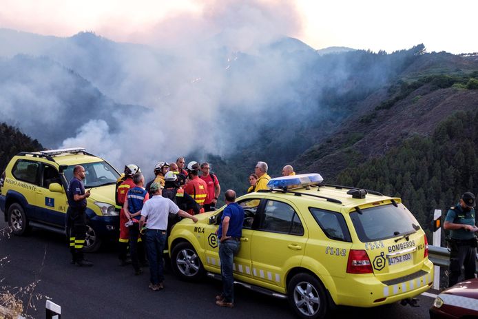 Hulpverleners en brandweermannen overleggen op Gran Canaria terwijl achter hen het vuur voortraast.