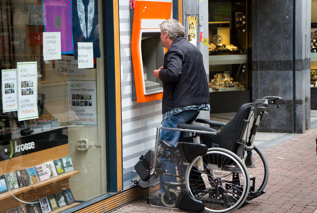 Een man staat op uit zijn rolstoel om geld te pinnen bij een pinautomaat van in Arnhem. Pinautomaten zijn voor veel gehandicapten moeilijk toegankelijk.
 Beeld Hollandse Hoogte