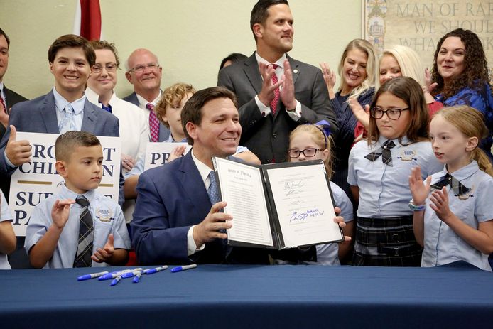 Gouverneur Ron DeSantis toont de zojuist door hem ondertekende wet, terwijl hij is omringd door basisschoolkinderen in een school in Shady Hills, Florida.