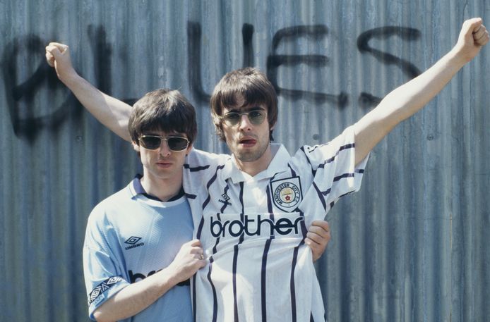 Gitarist Noel Gallagher (links) en zijn broer, zanger Liam Gallagher, van de Britse rockband Oasis op archiefbeeld uit 1994. Beiden in het shirt van hun favoriete voetbalclub Manchester City. © Getty Images