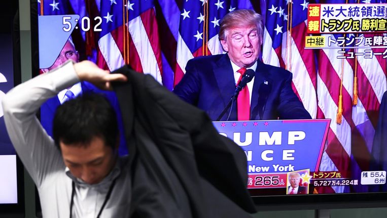 Een handelaar verlaat zijn werkplek in Tokio, terwijl Donald Trump op tv zijn overwinning opeist. Beeld AFP