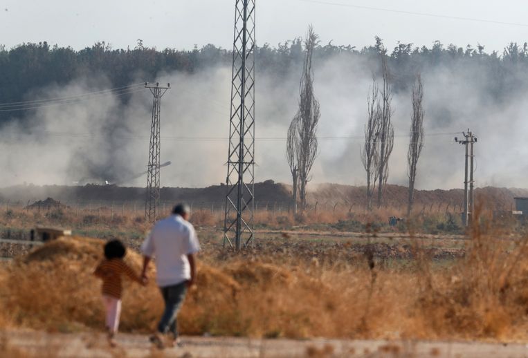 Mensen lopen in Akçakale in het zuidoosten van Turkije, terwijl op de achtergrond Turkse troepen vuren richting Syrië. Beeld AP