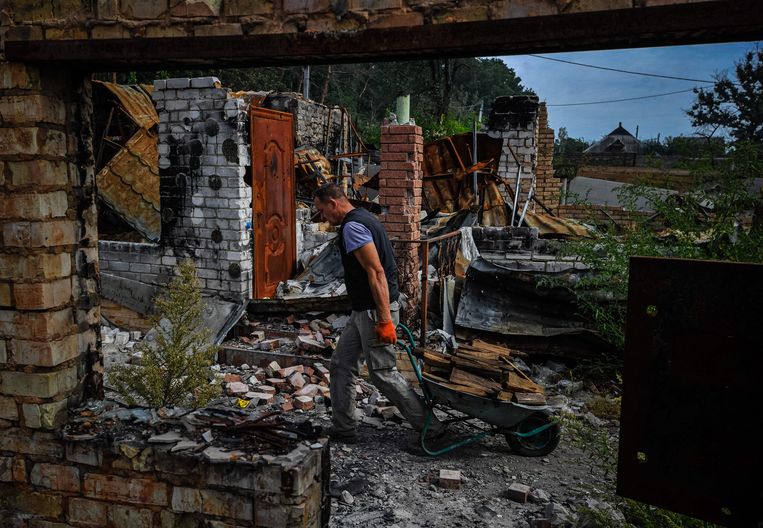 Een man sleept brandhout tussen de verwoeste huizen door van Mosjtsjoen, nabij Kiev.  Beeld AFP