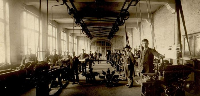 Leerlingen van de afdeling metaal van de Vrije Beroepsschool in de Menenstraat in Ieper poseren in hun werkplaats. (1927). Op de grond liggen twee rotatiemotoren van militaire vliegtuigen uit 1917.