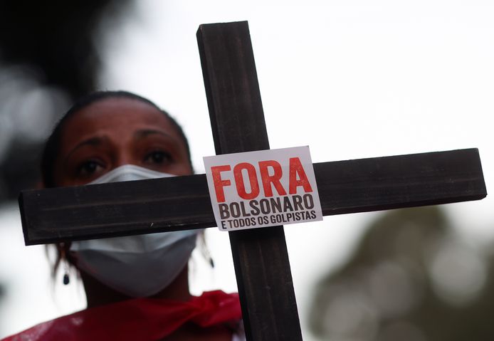 Een vrouw houdt een kruis omhoog met de tekst ‘Bolsonaro buiten’ bij een protestactie om de 100.000 Braziliaanse coronadoden te herdenken.