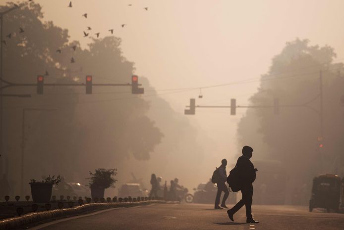 Forenzen steken een straat over te midden van smog in New Delhi.