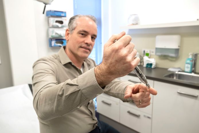Huisarts Luc Frenken demonstreert op zijn vinger hoe het hogedrukspuitje bij een sterilisatie werkt: het verdovingsmiddel wordt door de huid heen gespoten.