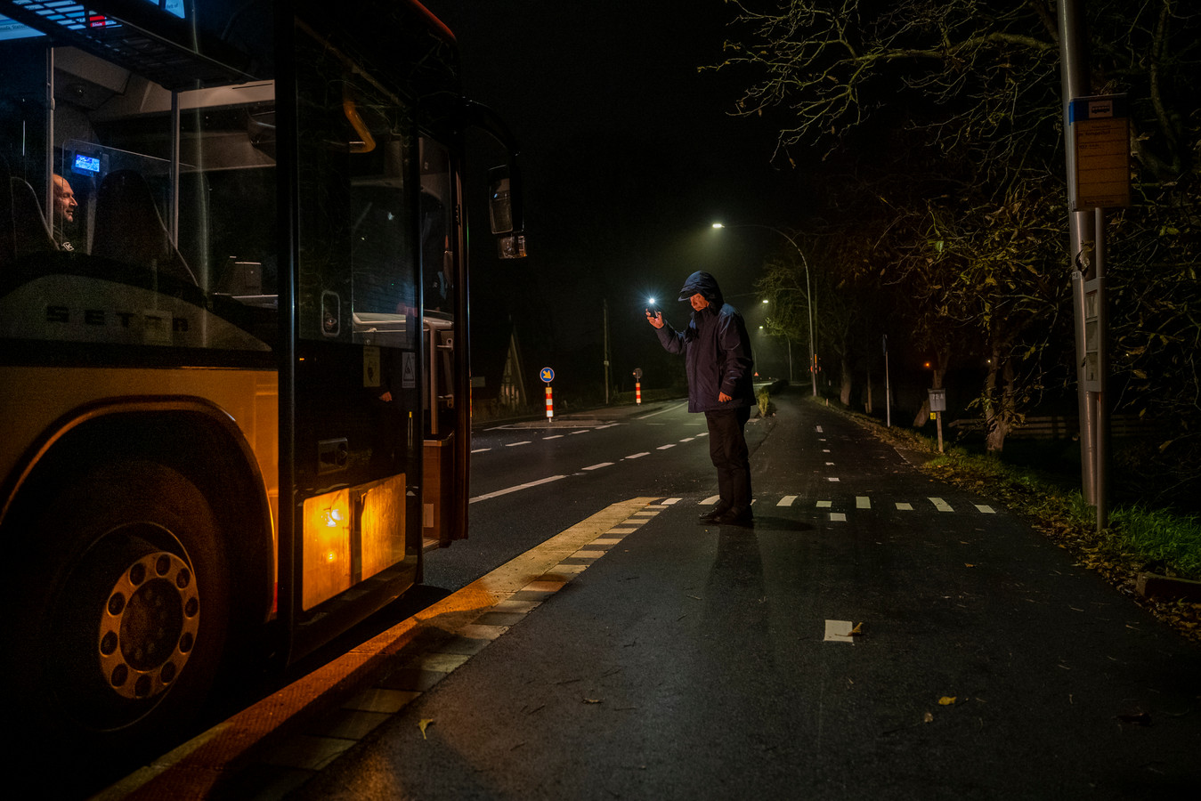 Een wachtende passagier trekt zwaaiend met zijn mobieltje de aandacht van de buschauffeur.