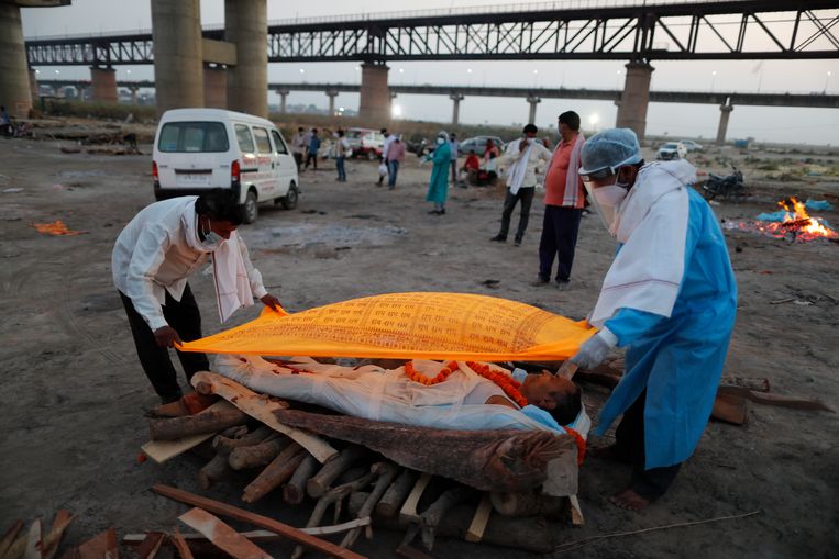 Twee mannen in de Indiase stad Prayagraj dekken het lichaam af van een aan covid overleden familielid voor de crematie bij rivier de Ganges. Beeld Rajesh Kumar Singh / AP