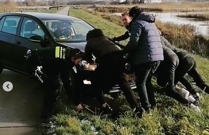 Vijf jongeren helpen agenten uit Arnhem en Overbetuwe een politieauto uit de modder te duwen.