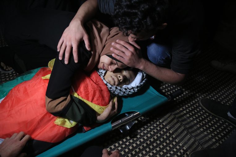 Nagham Tolbeh neemt haar broer Mahmoud (12) voor de allerlaatste keer vast. Hij maakte vaak eten klaar voor zijn broertjes en zusjes, zei zijn vader. 'Mahmoud wilde ingenieur worden. Hij had een rooskleurige toekomst. Maar die werd gelijk met hem begraven’, zegt Hamed Tolbeh, zijn vader. Beeld NYT/SAMAR ABU ELOUF