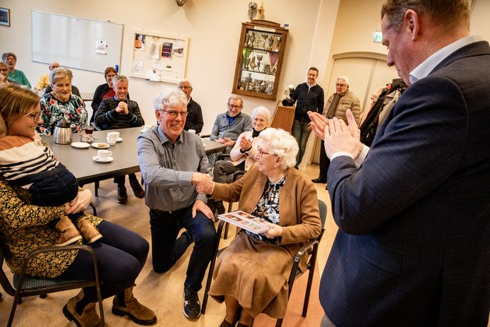 Amateurfotograaf Ger Jansens (op zijn knie) is de initiatiefnemer van het boek ‘80’ers vertellen’. Burgemeester Jos van Bree (helemaal rechts) overhandigde het eerste exemplaar aan de eerste deelnemer van het project, Marieke van der Heijden (op de stoel).