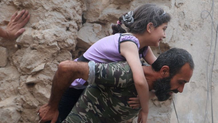 Een Syrische man draagt een gewond meisje in Aleppo. Luchtaanvallen in het noordwesten van Syrië hebben vrijdag aan zeker 23 mensen het leven gekost. Beeld reuters