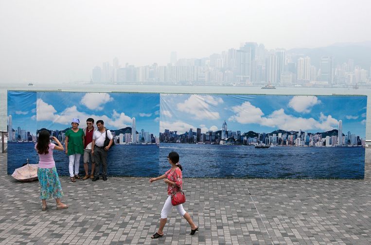 Toeristen nemen een foto voor een doek waarop Hong Kong is afgebeeld op een heldere dag. Daarachter het echte Hong Kong, op een dag in augustus 2013. Beeld EPA