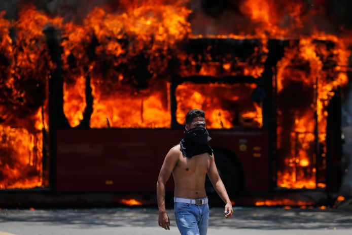 Een demonstrant loopt in Caracas voor een bus langs die in brand is gestoken door demonstranten.