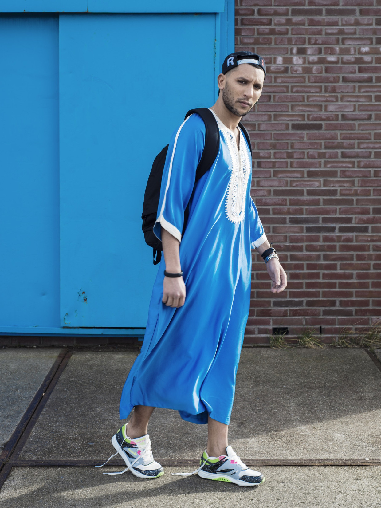 Kandora (Essaouira), sneakers (Reebok Ventilator Vintage), Pet (Reebok), rugzak (Nike), horloge (Rolex), leren armband (Hermès), zwarte armband (Nike). Beeld Robin de Puy
