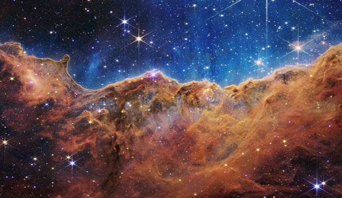 Een landschap van "bergen" en "valleien”, gespikkeld met glinsterende sterren dat eigenlijk de rand is van een nabijgelegen, jong, stervormingsgebied genaamd NGC 3324 in de Carina Nevel.