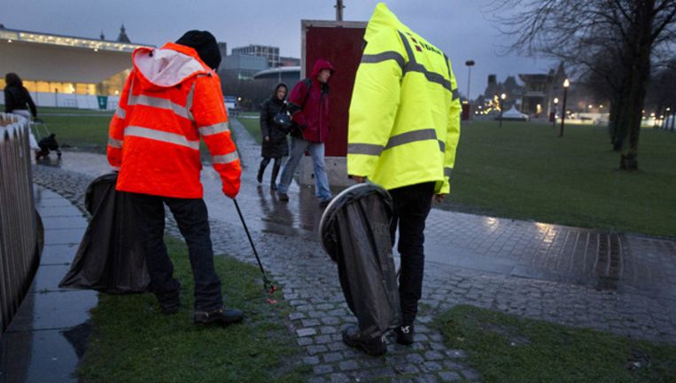 Twee personen die zich tijdens de jaarwisseling hadden misdragen tijdens de jaarwisseling, ruimen afval op het Museumplein in Amsterdam. © ANP Beeld 