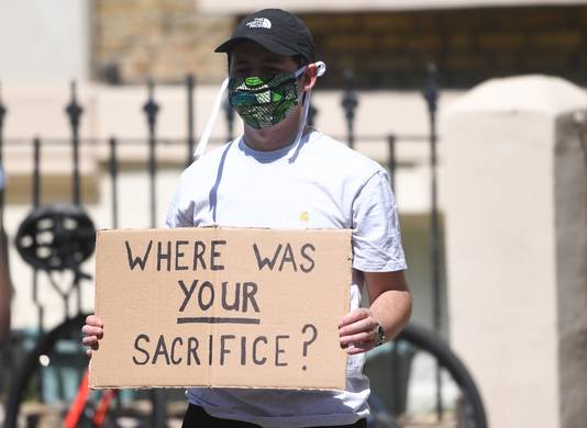 Een demonstrant die een gezichtsmasker draagt, houdt een protestbord vast voor het huis van Dominic Cummings.