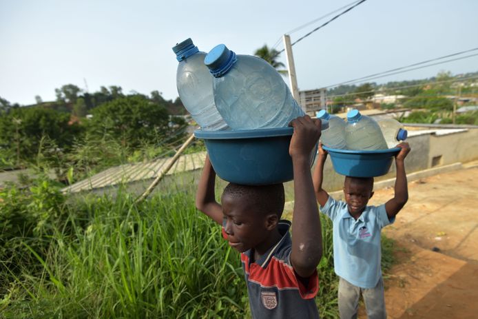 Twee kinderen komen terug van een waterbron met een aantal gevulde flessen water in de dichtbevolkte wijk Yopougon, in de stad Abidjan in de Ivoorkust.