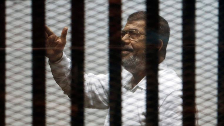 De afgezette Egyptische president Mohamed Morsi zwaait tijdens zijn proces naar zijn aanhangers. Beeld REUTERS