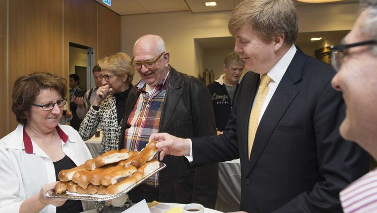 Koning Willem-Alexander krijgt een worstenbroodje aangeboden tijdens een bezoek aan woonzorgcentrum Fendertshof in Fijnaart. Beeld anp
