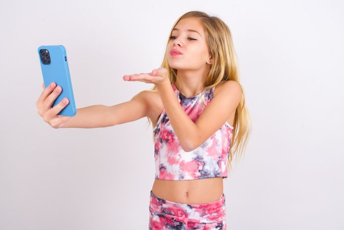 Een meisje werpt een handkus richting de camera van een smartphone en neemt een selfie. Veel ouders hebben er geen moeite mee om zulke foto's te delen op hun account.