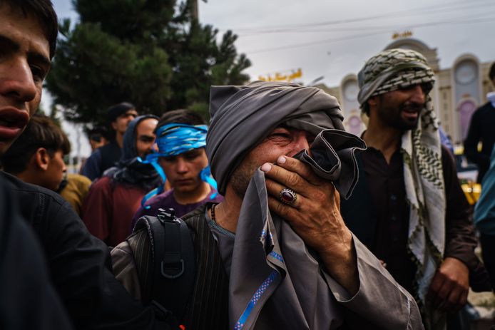 Een Afghaanse man kijkt vol afschuw naar talibanstrijders die met vuurwapens, zwepen en stokken de menigte te lijf gaan in de buurt van de internationale luchthaven in Kaboel.