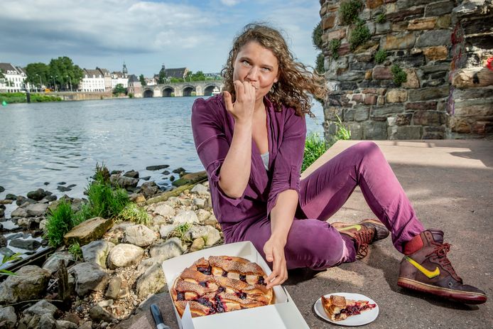 Culinair journaliste Laura de Grave, met streekproduct Limburgse vlaai van de Bisschopsmolen, langs de Maas in Maastricht met op de achtergrond de oude Maasbrug.