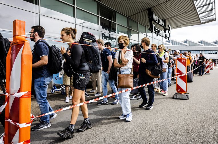 Passagiers wachten binnen en buiten de vertrekhallen op Schiphol in lange rijen voor de paspoortcontrole.  Beeld ANP / Jeffrey Groeneweg