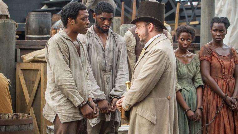 Slavenhandelaar Theophilus Freeman, gespeeld door Paul Giamatti, bekijkt slaaf Solomon Northup (Chiwetel Ejiofor) op een slavenmarkt. Beeld Het Parool