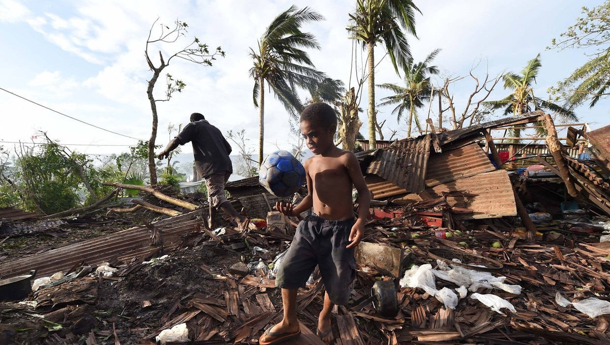 Een jongen speelt met een bal terwijl zijn vader zoekt in de ruïnes van hun huis in Port Vila ,de hoofdstad van het eilandje Vanuatu Beeld afp