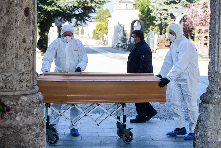 Begrafenisondernemers in beschermende kleding verplaatsen een kist bij een begraafplaats in Bergamo.  Beeld AFP