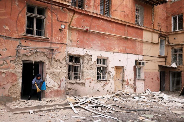 Een vrouw ruimt puin bij haar appartement in Cherson dat zwaar beschadigd is geraakt bij een Russische aanval. Beeld REUTERS