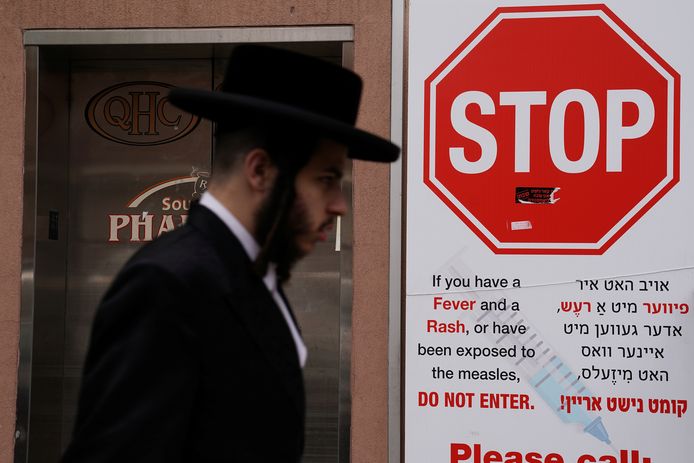 Een Joodse man loopt langs een waarschuwingsbord voor de mazelen.