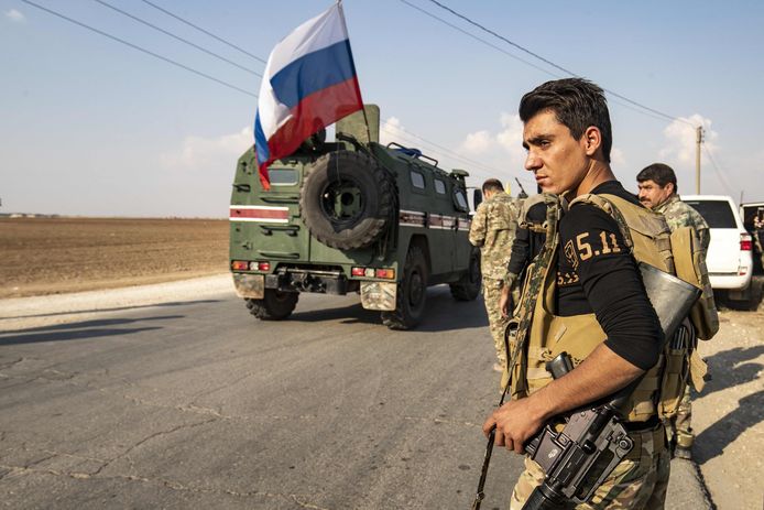 SDF-strijders maken zich op om zich terug te trekken, terwijl een Russisch legervoertuig voorbij rijdt.