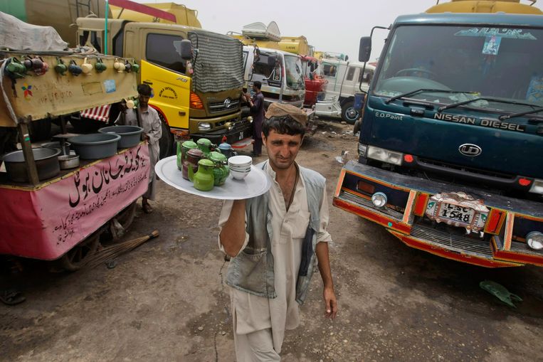 Een theeverkoper wandelt met zijn waar tussen de geparkeerde vrachtwagens door in Karachi om kopjes thee te verkopen.  Beeld AP