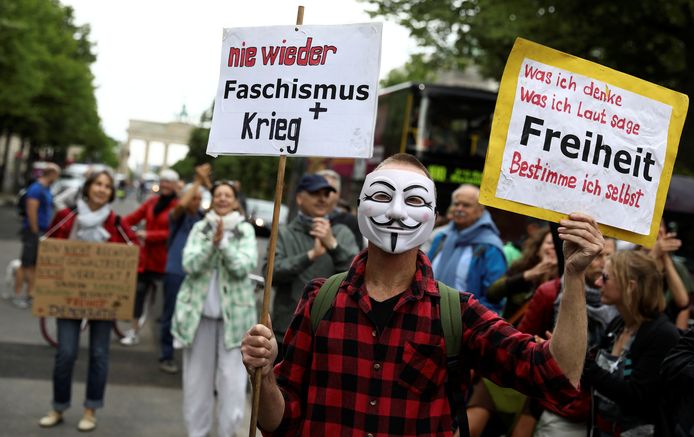 Een demonstrant in Berlijn draagt een masker en een bord met de teksten "Nooit meer fascisme en oorlog" (links) en "Wat ik denk, wat ik luidop zeg, vrijheid bepaal ik zelf" (rechts).