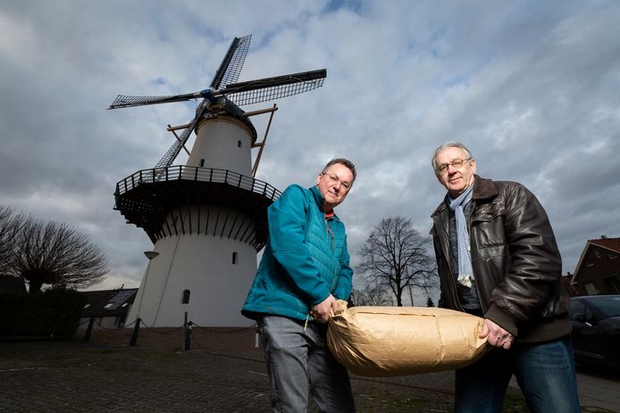 Cor Groen  (links) en Jacques Boonekamp van Stichting Molen De Hoop tillen een 25 kilozak meel.