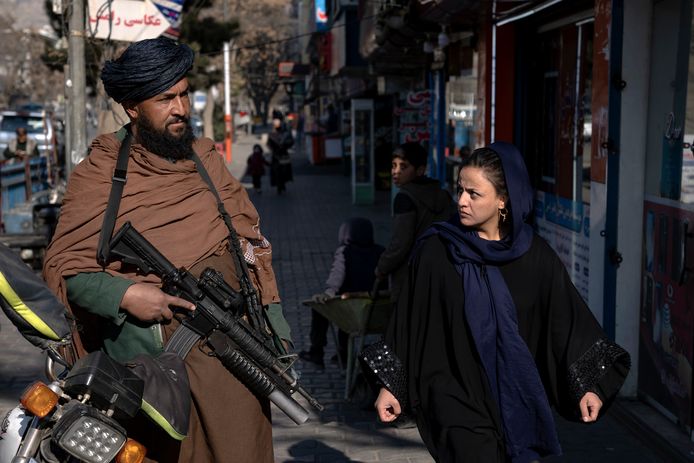 Een vrouw loopt langs een talibanstrijder in Kaboel, Afghanistan.