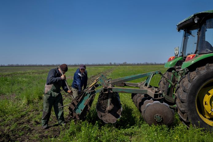 Twee boeren verwijderen modder van een tractor terwijl ze een veld proberen te oogsten in Potomkyne, regio Kherson, Oekraïne.