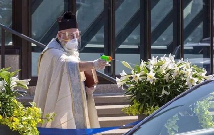Priester schiet wijwater op kerkgangers tijdens de pandemie.
