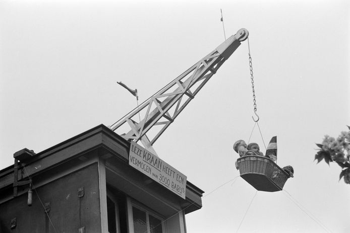 Een kraan draagt symbolisch de 3,000 baby’s die verloskundige mevrouw Ria Gielen-Kraan in 25 jaar in Berghem hielp geboren worden (1957). Het bord zegt: ' Deze kraan heeft een vermogen van 3000 babay's'.