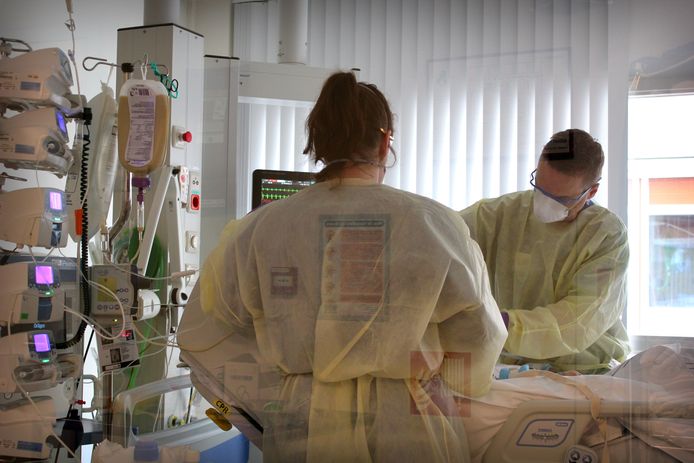 Twee verpleegkundigen in een ic-kamer. De kamers zijn afgesloten; daarom is de foto vanaf de gang en door het glas gemaakt.