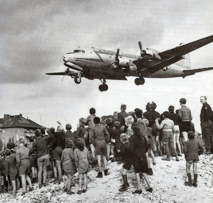 Inwoners kijken toe hoe een Amerikaans transportvliegtuig de Sovjetblokkade van West-Berlijn doorbreekt in 1948