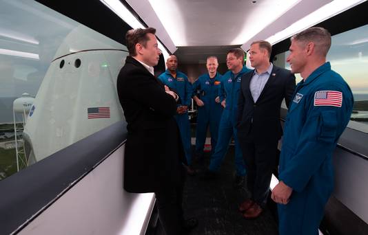 SpaceX-ceo Elon Musk (links), astronauten Victor Glover, Doug Hurley, Bob Behnken, Nasa-directeur Jim Bridenstine, en astronaut Mike Hopkins staan in de arm die toegang verleent tot de Crew Dragon tijdens een tour van de lanceerlocatie voorafgaang aan de onbemande 'Demo 1'-missie in 2019.
