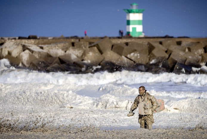 Een reddingswerker waadt door het schuim aan de kust bij Scheveningen.